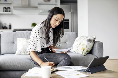 Woman sitting on couch and working on paperwork and tablet